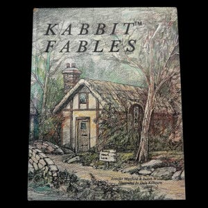 May include: A book cover with the title "KABBIT FABLES" above an illustration of a cottage. The cottage has a thatched roof, a chimney, and a small sign that reads "Rabbit Heart Lane". The artwork is in a pencil sketch style.