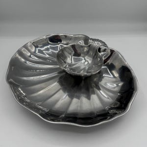 May include: A silver serving dish set. The set comprises a large, shell-shaped platter and a smaller, attached bowl. The platter features a fluted design, and the bowl has a handle. The set is made of a shiny metal.
