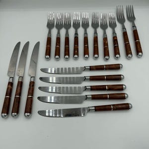 May include: A set of stainless steel forks and knives with dark brown wooden handles. The forks have four tines, and the knives have serrated blades. The handles are cylindrical with a silver metal band at the base.