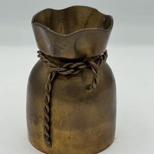 May include: A small, antique-style bronze vase. The vase has a rounded body and a ruffled top, with a twisted rope detail around the middle. The bronze has a warm, aged patina. The vase is approximately 10 cm tall.