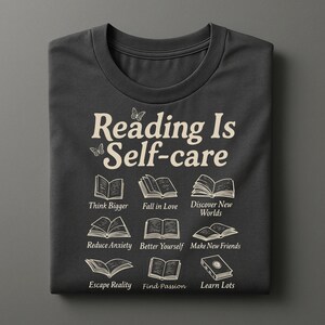 Puede incluir: Camiseta gris oscuro con el texto "Reading Is Self-care" e ilustraciones de libros. Debajo, las frases "Think Bigger", "Fall in Love", "Discover New Worlds", "Reduce Anxiety", "Better Yourself", "Make New Friends", "Escape Reality", "Find Passion" y "Learn Lots".