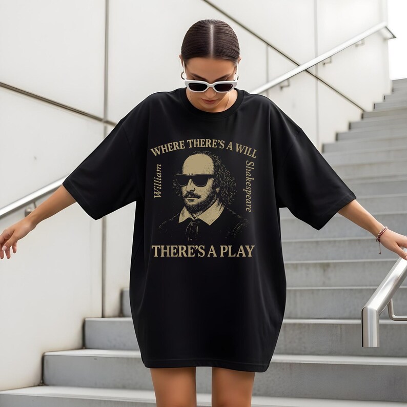 May include: Black oversized t-shirt with a graphic of William Shakespeare in sunglasses. The text reads "WHERE THERE'S A WILL THERE'S A PLAY", with "William" and "Shakespeare" on either side. The shirt is being worn by a person.