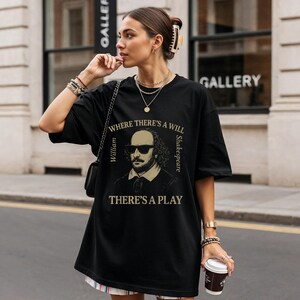May include: Black t-shirt with a vintage-style graphic of William Shakespeare in sunglasses, and the text "WHERE THERE'S A WILL THERE'S A PLAY." The shirt is worn by a person.
