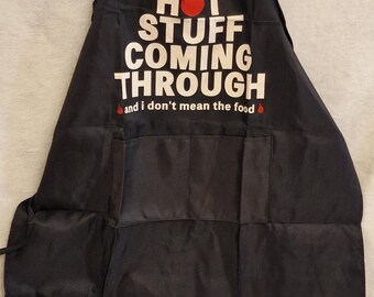 May include: Black apron with the text "HOT STUFF COMING THROUGH" in white, with a red flame graphic. The apron has pockets and adjustable neck and waist straps.