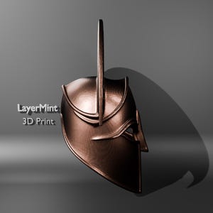 Puede incluir: Un casco de color bronce con una espiga vertical alta que se extiende desde la parte superior. El casco tiene una superficie detallada y texturizada y un dise&ntilde;o curvo, con el texto "LayerMint 3D Print" visible en el lado izquierdo. El casco proyecta una sombra sobre un fondo gris.