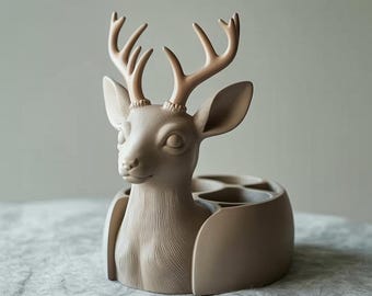 May include: A decorative deer-shaped container in a neutral beige color. The deer has detailed antlers and a textured face. The container has multiple compartments, suitable for holding small items. The design is modern and artistic.