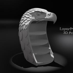 May include: A gray, 3D-printed shelf unit shaped like an eagle's head. The eagle's head has detailed feather and eye features. The shelf unit has four circular shelves inside the eagle's head. The text "LayerM 3D Print" is visible on the right side.