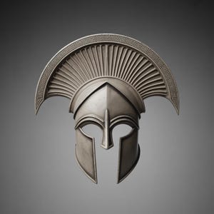 Puede incluir: Un casco espartano plateado con una cresta decorativa y aberturas para los ojos. El casco tiene un dise&ntilde;o detallado, con una parte superior curvada y una protecci&oacute;n facial. El fondo es gris liso.
