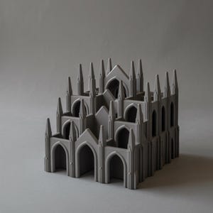 May include: A gray, architectural model of a cathedral. The model features multiple arched doorways, pointed spires, and a layered design. The overall aesthetic is minimalist and modern, with a focus on geometric shapes and clean lines.