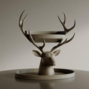 Puede incluir: Escultura decorativa de cabeza de ciervo en color topo. La escultura presenta una bandeja sostenida por las astas y una base circular. La cabeza del ciervo está detallada, creando un acento decorativo único para el hogar.
