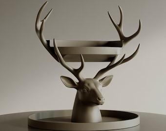 May include: A decorative deer head sculpture in a neutral taupe color. The sculpture features a tray supported by the antlers and a circular base. The deer head is detailed with realistic features, creating a unique home decor accent.