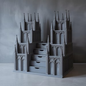 Peut inclure: Unité de rangement grise de style gothique avec de multiples flèches et fenêtres cintrées. L'unité comporte quatre tiroirs et une conception en gradins, ressemblant à une cathédrale miniature. Le design général est symétrique et détaillé.