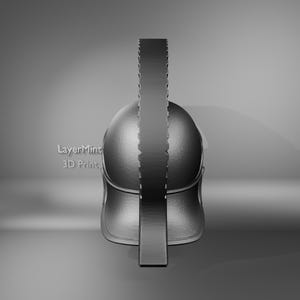 K&ouml;nnte beinhalten: Ein 3D-gedruckter, metallisch aussehender spartanischer Helm, von vorne betrachtet. Der Helm hat eine abgerundete Oberseite und einen vertikalen Kamm mit geriffeltem Design. Der Text "LayerMint 3D Print" ist sichtbar.