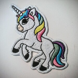 Può includere: Toppa ricamata di un unicorno bianco con criniera e coda arcobaleno. L'unicorno ha un occhio nero e un corno nero. La toppa è bordata di bianco e nero.