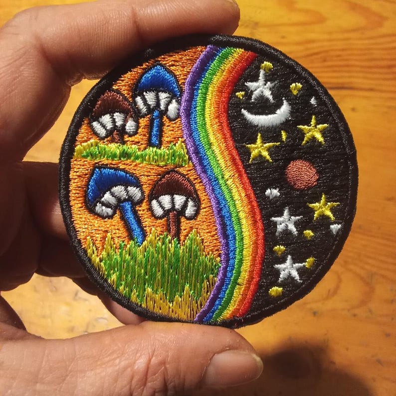 Peut inclure: &Eacute;cusson brod&eacute; rond avec un motif divis&eacute;. Un c&ocirc;t&eacute; pr&eacute;sente des champignons, de l'herbe et un arc-en-ciel. L'autre c&ocirc;t&eacute; montre un ciel nocturne avec des &eacute;toiles, un croissant de lune et une plan&egrave;te. Bordure noire.