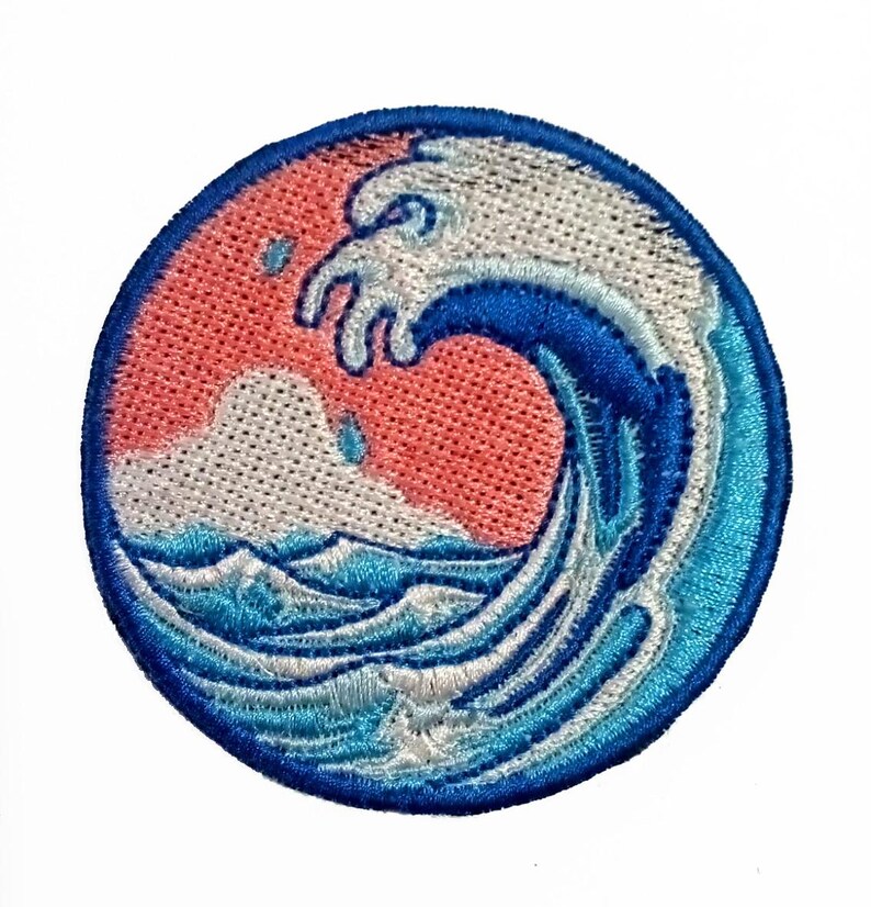 May include: An embroidered patch depicting a blue and white wave crashing over a pink and white sunset. The wave is blue with white foam and the sunset is pink with white clouds.