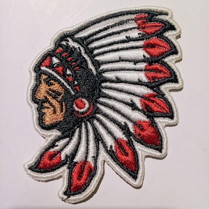 Può includere: Toppa ricamata raffigurante un capo nativo americano di profilo, con un copricapo. La toppa ha uno sfondo bianco con dettagli neri e rossi. Il volto del capo è color bronzo e il copricapo ha piume rosse.