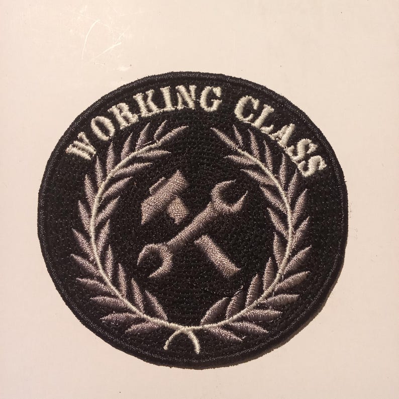 Può includere: Toppa rotonda nera con la scritta bianca "WORKING CLASS" ad arco nella parte superiore. All'interno, un martello e una chiave inglese si incrociano, circondati da una corona d'alloro grigia. Adatta da cucire su abbigliamento o accessori.