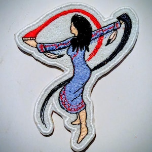 Può includere: Toppa ricamata raffigurante una donna in abito blu con dettagli rossi e neri, con le braccia tese. La toppa ha un bordo bianco e raffigura una figura stilizzata con lunghi capelli neri. Il disegno comprende un arco rosso e un arco nero.