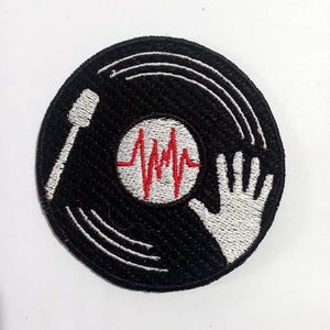 Op de afbeelding: Zwart-witte geborduurde patch van een vinylplaat met een rode hartslaggrafiek en een witte hand die naar de plaat reikt.
