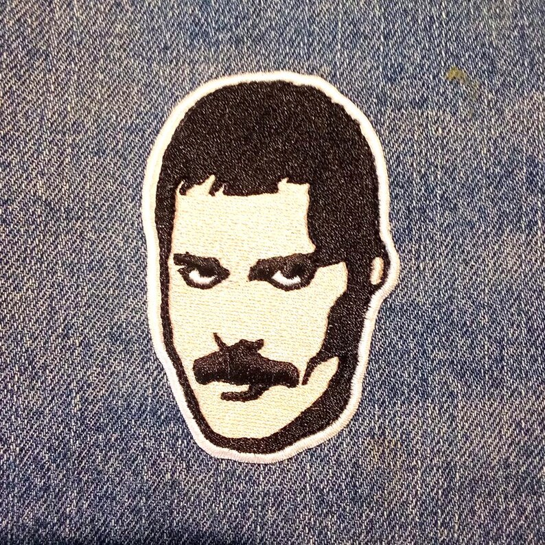 Op de afbeelding: Geborduurde patch met een zwart-wit portret van een man met een snor. De patch heeft een witte rand en is geplaatst tegen een blauwe denim achtergrond. Het portret is een gestileerde weergave.