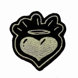Può includere: Toppa ricamata con un cuore, alone e contorno nero. Il cuore è grigio chiaro e il design circostante è nero. La toppa ha un bordo decorativo, adatta per abbigliamento o accessori.