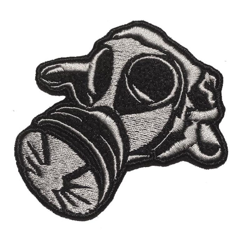 May include: Embroidered patch featuring a gas mask design. The patch is primarily black and gray, with detailed stitching that outlines the mask's features. The design is a stylized representation of a gas mask.