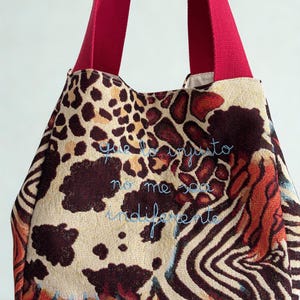 May include: Tote bag with a vibrant animal print design featuring leopard spots and zebra stripes. The bag has bright red straps and embroidered text in blue. A stylish and functional accessory.