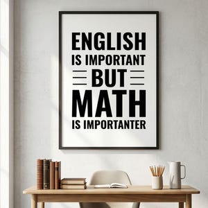 May include: A framed print with the text "ENGLISH IS IMPORTANT BUT MATH IS IMPORTER". The black framed print hangs above a wooden desk with books, a chair, and a white pitcher. The room has a window and a neutral color scheme.