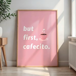 Könnte beinhalten: Gerahmtes rosa Wandbild mit dem Text "but first, cafecito." Eine rosa Kaffeetasse mit Herzen ist abgebildet. Das Kunstwerk wird in einem Raum mit einem hölzernen Beistelltisch und einer weißen Vase mit Grünpflanzen ausgestellt.