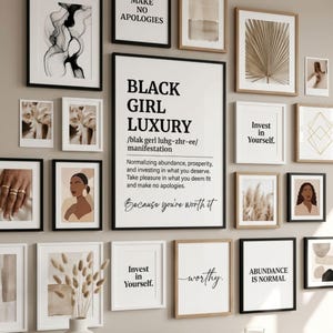 May include: A gallery wall arrangement featuring various framed prints, including a central poster with the text Black Girl Luxury, definition, and manifestation, alongside prints with phrases like Invest in Yourself and Abundance is Normal.