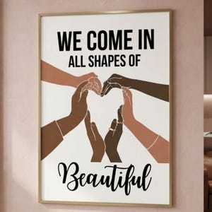 May include: Framed art print with the words "WE COME IN ALL SHAPES OF Beautiful". The artwork features hands of various skin tones forming a heart shape. The frame is gold.