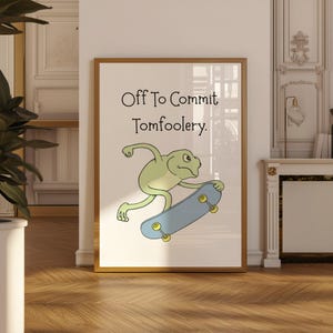 May include: A framed art print with a cartoon frog on a skateboard. The frog is light green, and the skateboard is blue with yellow wheels. The text "Off To Commit Tomfoolery" is above the frog.