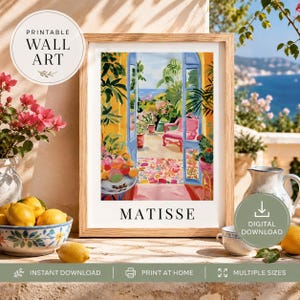 May include: A framed art print titled MATISSE featuring a colorful Mediterranean balcony scene with blue doors, a pink chair, lush green plants, and a bowl of fruit. The artwork is displayed in a light wood frame with a white border.