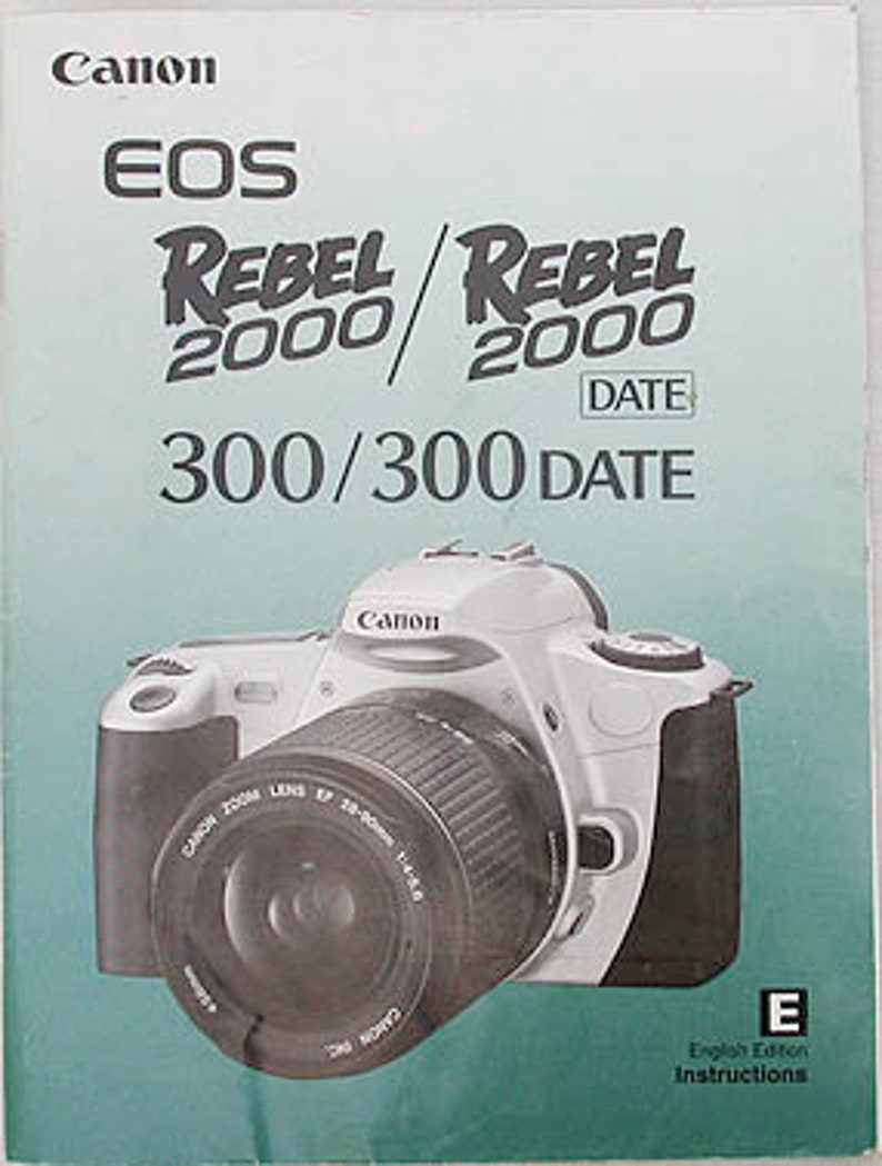 May include: A white Canon EOS Rebel 2000/2000 Date 300/300 Date camera with a Canon Zoom Lens EF 28-80mm 1:4-5.6 attached. The camera has a black lens cap and a black strap.