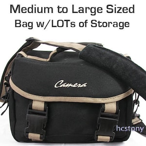 May include: Black camera bag with a tan trim and the word "Camera" embroidered on the front. The bag has two adjustable straps and a zipper closure.