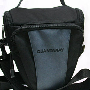 May include: Black and gray Quantaray camera bag with a top handle, shoulder strap, and multiple zippered compartments. The bag features the brand name "QUANTARAY" embroidered on the front. The bag is designed to carry and protect photographic equipment.