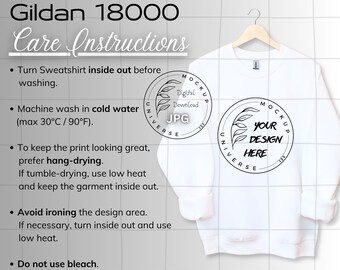 May include: A white Gildan 18000 sweatshirt hangs on a wooden hanger. The sweatshirt has a crew neck and long sleeves. The image includes care instructions and two circular logos with the text "MOCKUP UNIVERSE" and "YOUR DESIGN HERE".