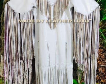 May include: A white leather dress with long sleeves and extensive fringe detailing. The fringe is a mix of light and dark shades, creating a layered effect. The text "MADE BY LEATHER LUXU" is visible on the dress.