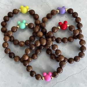 May include: Four wooden bead bracelets with colorful Mickey Mouse-shaped accents. The bracelets feature brown wooden beads and Mickey Mouse heads in yellow, green, red, and pink. Gold-colored beads are interspersed.