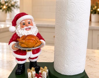 May include: A Santa Claus figurine paper towel holder on a dark green rectangular base. Santa wears a red and white suit, holding a silver platter with a roasted turkey. Three small gift boxes sit at Santa's feet next to a white paper towel roll.