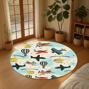 Op de afbeelding: Een rond vloerkleed met een crèmekleurige achtergrond met een patroon van vliegtuigen, helikopters, luchtballonnen, wolken en sterren in verschillende kleuren. Het kleed ligt op een houten vloer.