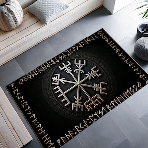 Puede incluir: Alfombra negra y dorada con un diseño de brújula y runas alrededor del borde. La brújula tiene un acabado plateado y está rodeada de un círculo negro con un borde dorado.