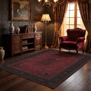 May include: A burgundy area rug with a black border and floral design. The rug is in a room with a dark wood floor, a red armchair, and a wooden cabinet. The room has a classic, elegant style.