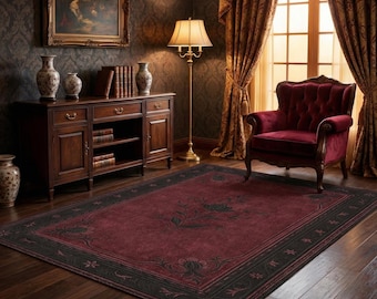 Puede incluir: Una alfombra burdeos con borde negro y diseño floral. La alfombra está en una habitación con suelo de madera oscura, un sillón rojo y un mueble de madera. La habitación tiene un estilo clásico y elegante.