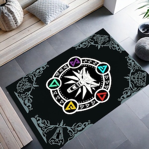 Puede incluir: Alfombra rectangular negra con un emblema de cabeza de lobo blanco rodeado de formas geom&eacute;tricas coloridas y un borde decorativo. La alfombra est&aacute; dise&ntilde;ada con un tema de juego y es adecuada para uso en interiores.