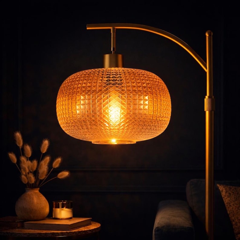 May include: A gold-toned floor lamp with a textured, amber-colored glass shade. The shade has a geometric pattern and emits a warm, inviting glow. The lamp is set against a dark background, creating a cozy ambiance.
