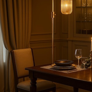 May include: A tall floor lamp with a slender metallic stand and a cylindrical, vertically ribbed glass shade that emits a warm glow. The lamp is positioned next to a wooden dining table set with stacked plates, a bowl, and glassware.
