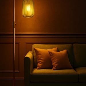 May include: A tall metal floor lamp with a slender stand and a rounded base, featuring a vertically ribbed, translucent yellow glass shade that emits a warm glow, positioned next to a green sofa with two matching orange square throw pillows.