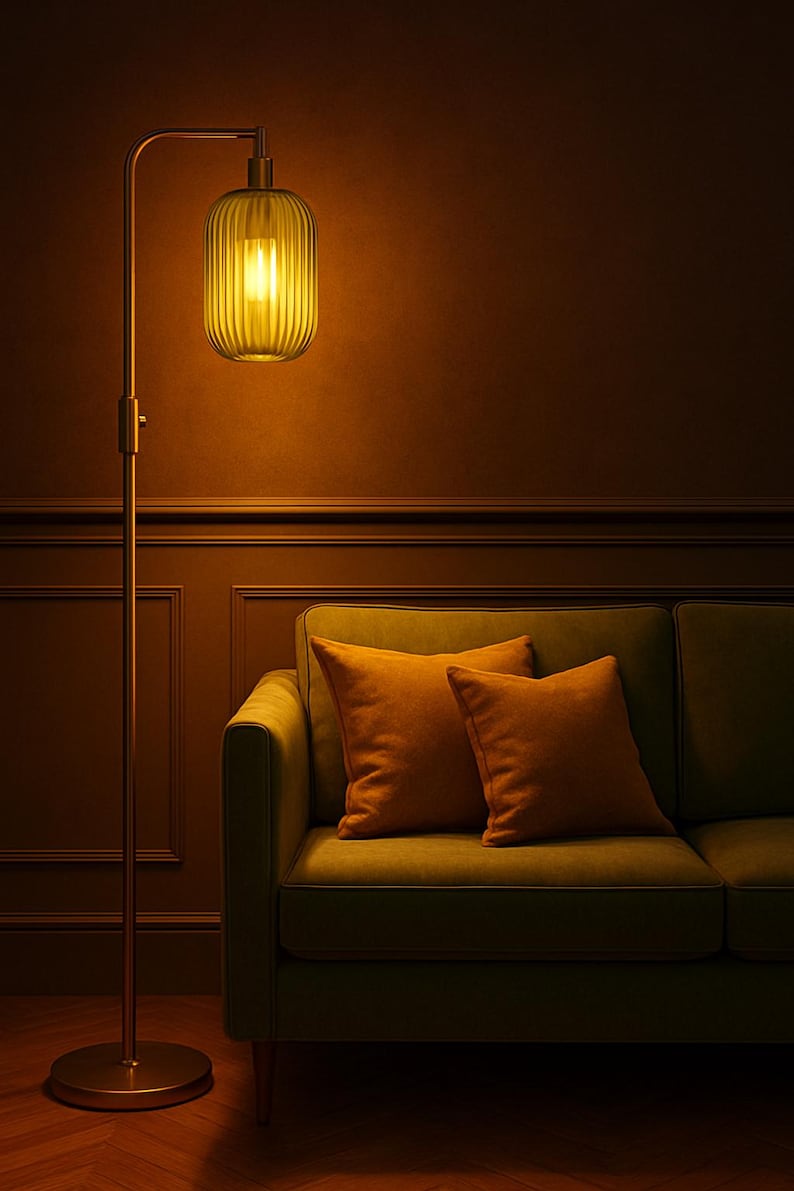 May include: A tall metal floor lamp with a slender stand and a rounded base, featuring a vertically ribbed, translucent yellow glass shade that emits a warm glow, positioned next to a green sofa with two matching orange square throw pillows.